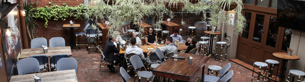 Outdoor restaurant patio with plants hanging and party of 8 dining.
