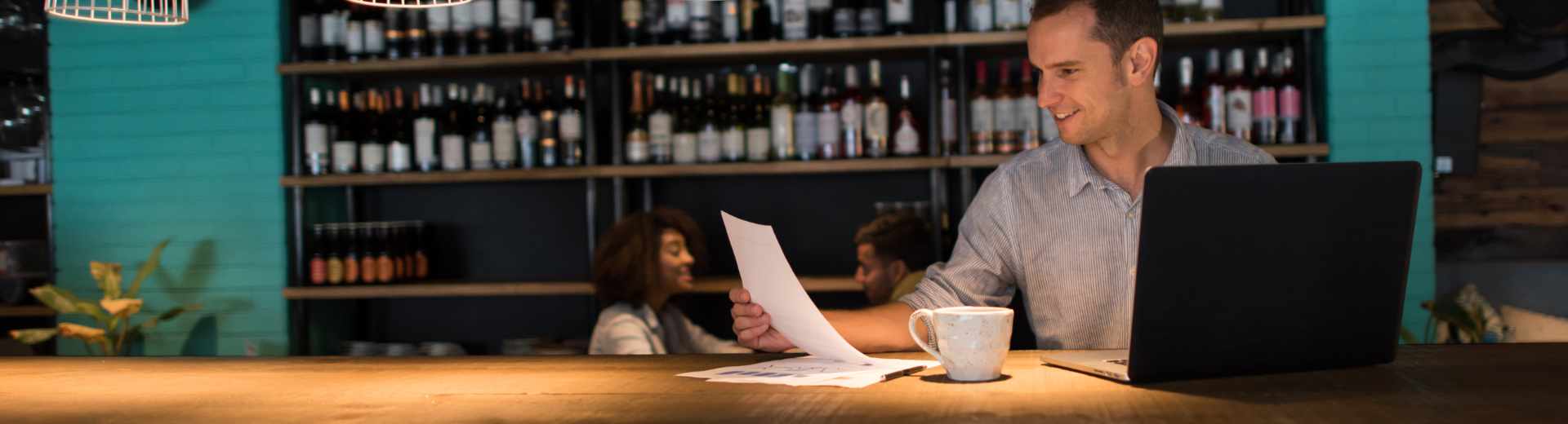 Restaurant manager sitting at bar looking at papers and laptop.