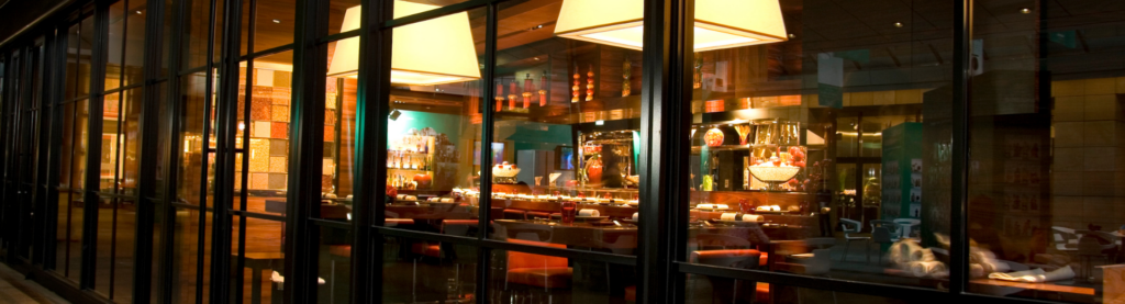 Exterior of a restaurant, looking into an empty dining room on a dark night.